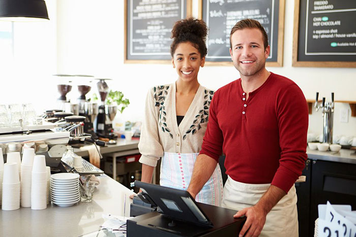 Two coffee bar employees posing in front of their POS system in their coffee shop.